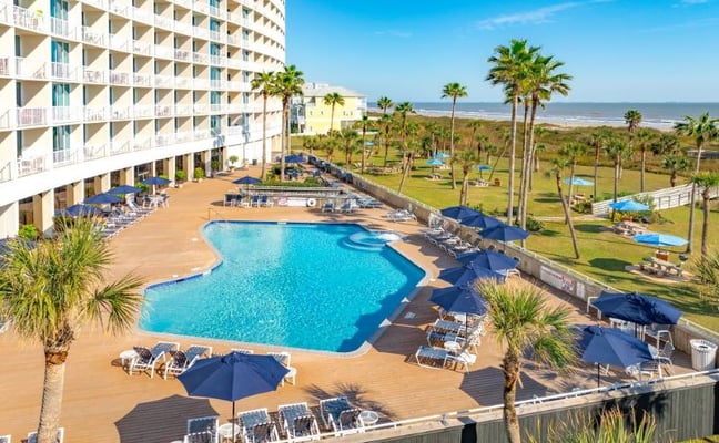 The Galvestonian pool deck with palm trees and Gulf views